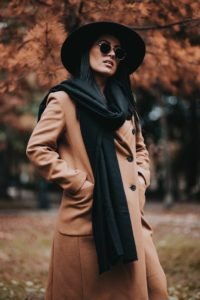 woman in brown coat and black hat standing near brown trees during daytime